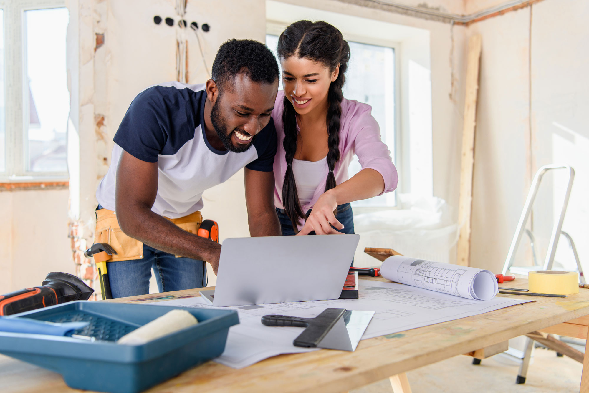 A young couple looking at a computer while renovating their home.